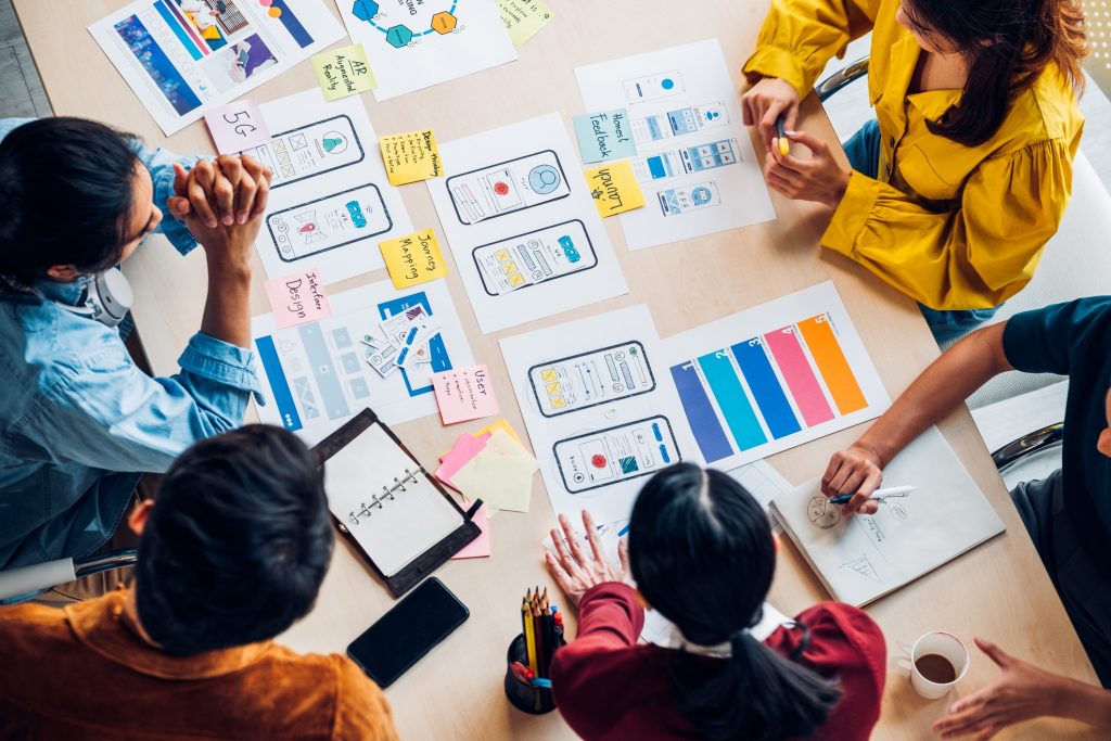 top view asian ux developer and ui designer brainstorming about mobile app interface wireframe design on table with customer brief and color code at modern office.Creative digital development agency, app development, custom software